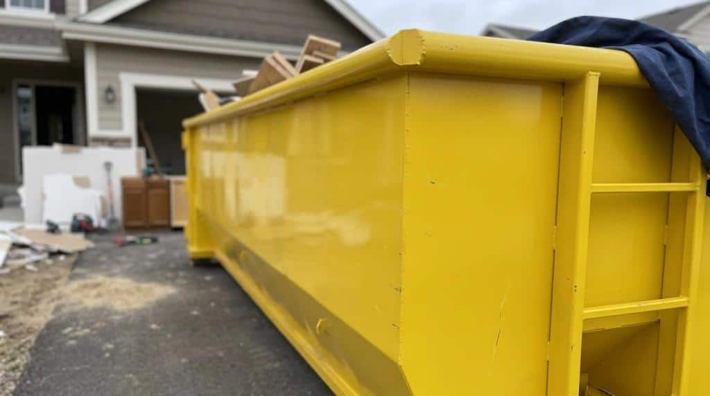 Yellow dumpster for construction debris in driveway.