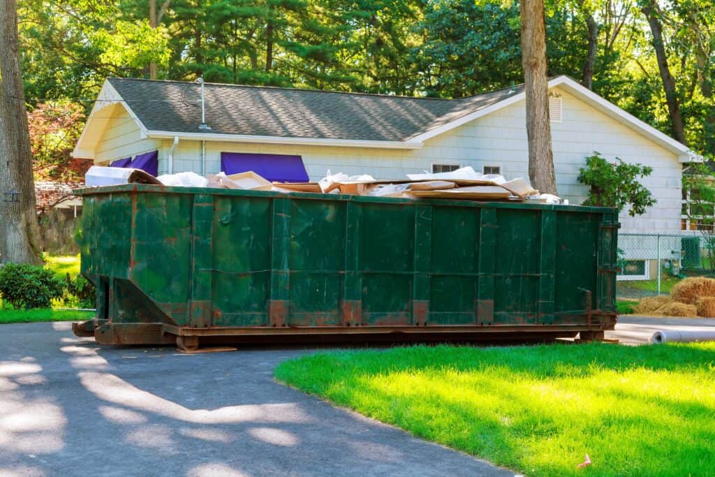 Dumpster Rental in Waverly, IA 1 Large green dumpster filled with construction debris in a residential yard.