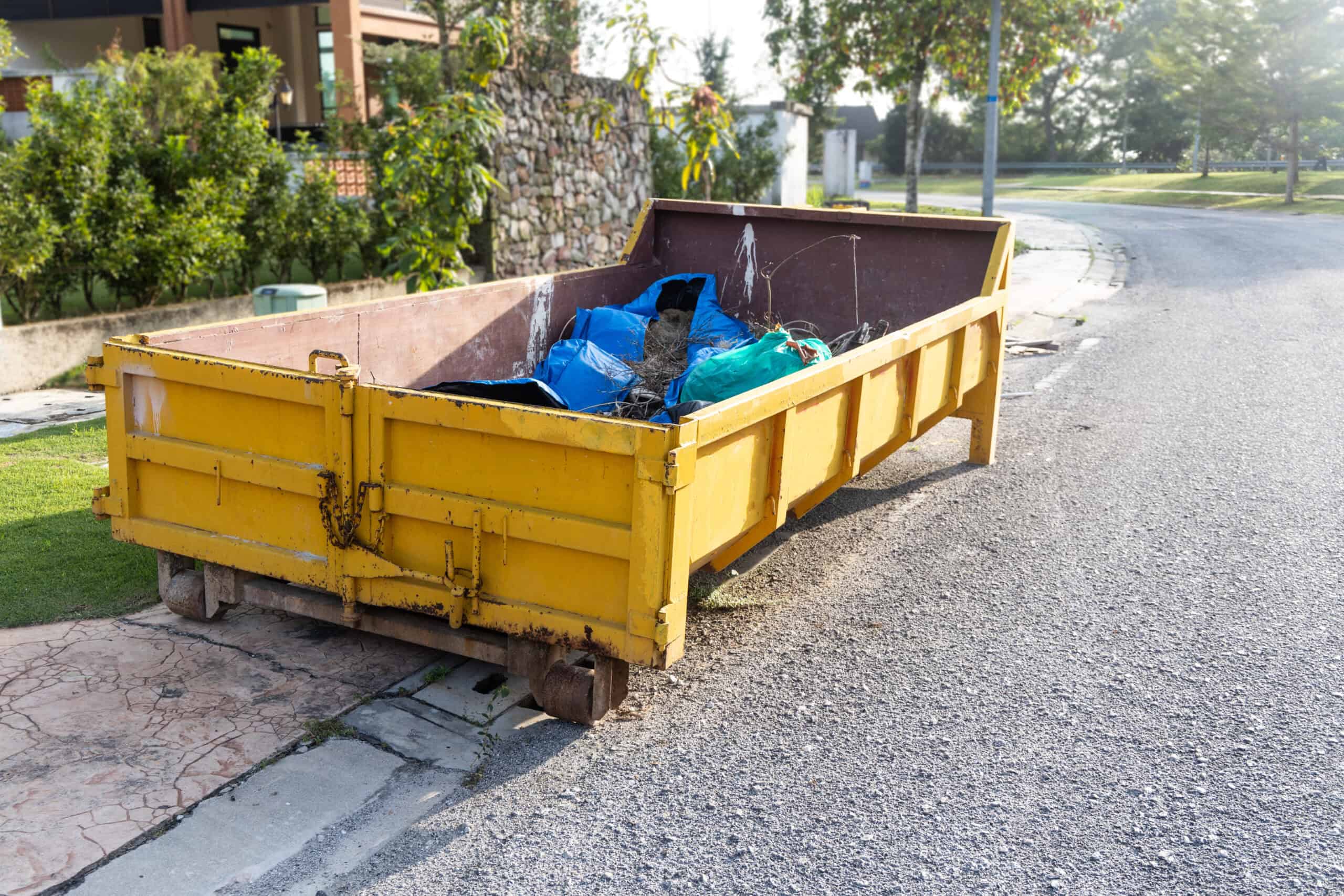 Dumpster Dimensions and How Much Space You Need 1 Yellow dumpster filled with trash bags on a street corner.