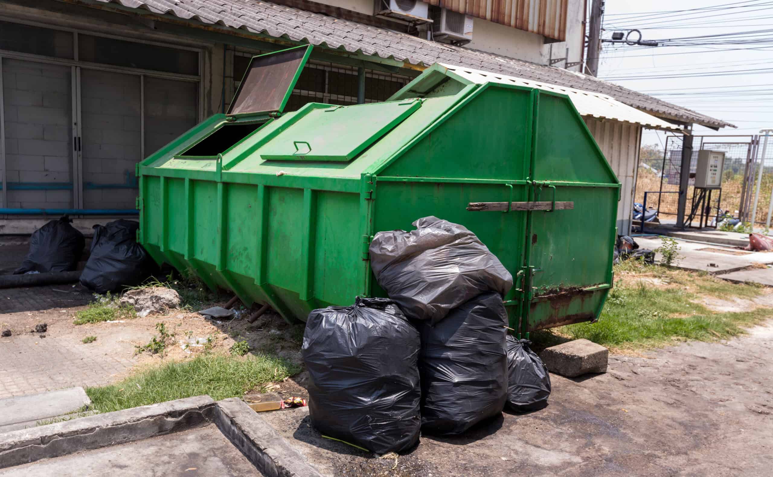 Large green dumpster with black trash bags outside a building.
