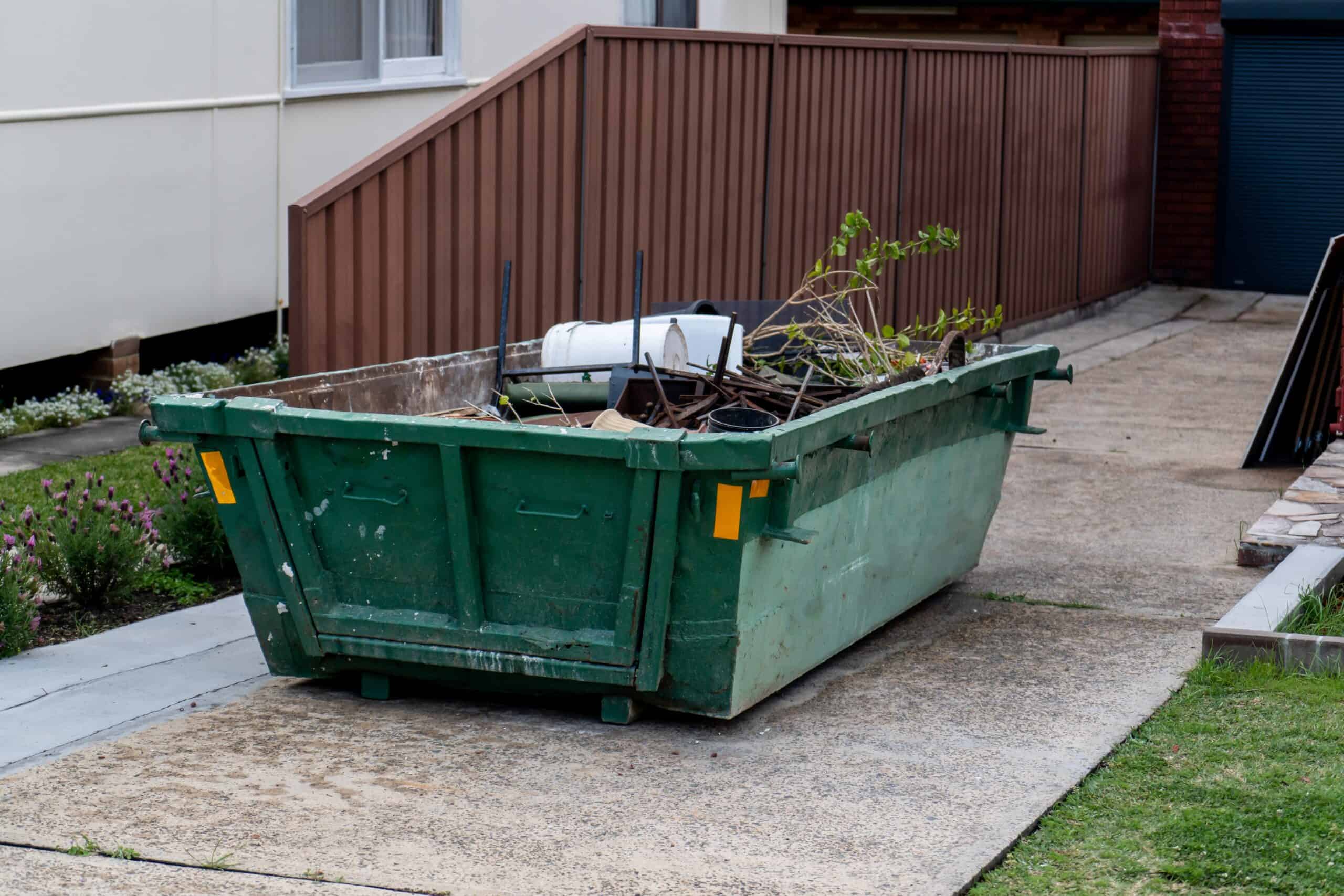 Green waste dumpster filled with debris outside residential property.